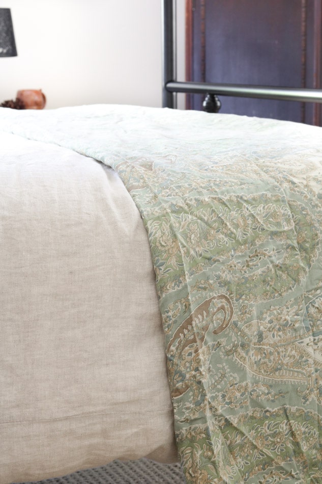 Linen duvet over with paisley throw folded at the end of the a bed in a cottagecore bedroom