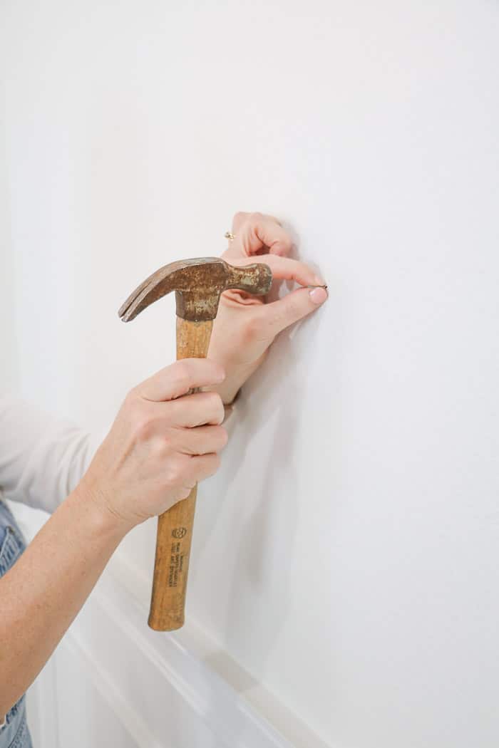 How to hang a gallery wall showing how to hammer a nail into the wall.