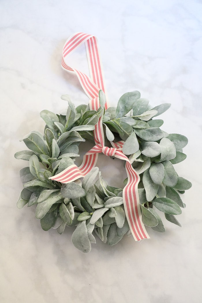 How to hang a wreath with ribbon on a window.  This simple DIY will show you two ways to hang wreaths on windows inside your home.  On this step tie the ribbon in a sailors knot where you marked with a pin.