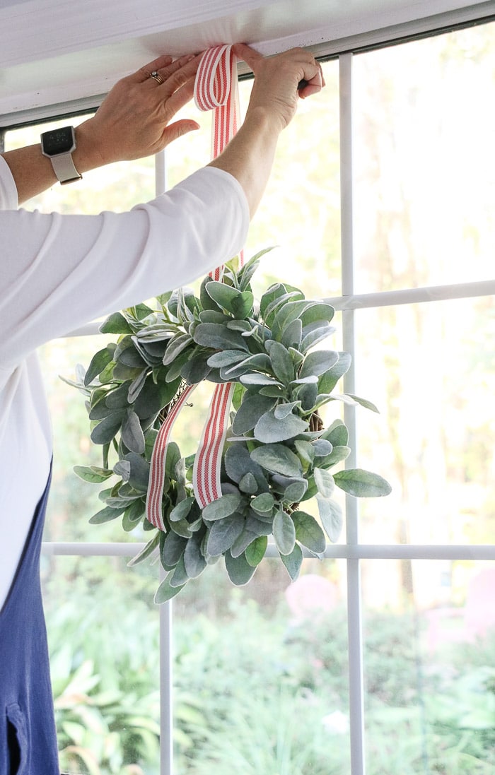How to hang a wreath with ribbon on a window.  This simple DIY will show you two ways to hang wreaths on windows inside your home.  On this step tape the ribbon to the top of the window seal.