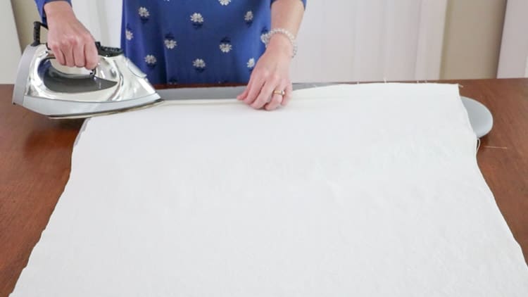 How to make a drop cloth rug by folding the canvas over the iron on hem tape and pressing the iron down for 3 to 5 seconds to close the hem