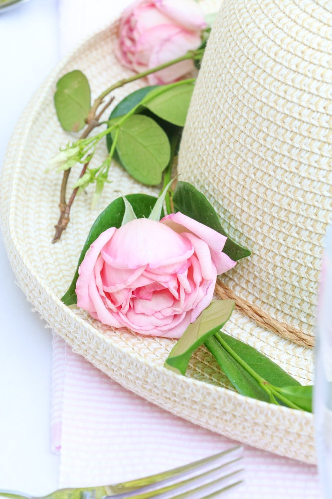 Garden party decoration ideas using a straw hat as a centerpiece with fresh green vine around the brim of the hat and fresh pink roses.