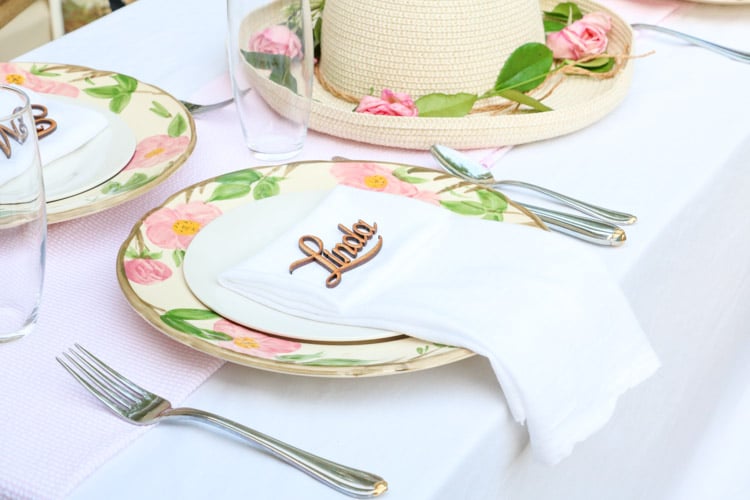 Garden party decoration ideas with a straw hat centerpiece, desert rose dishes, fine linens of pink and white, and laser cut letters of name of guest at each place setting.