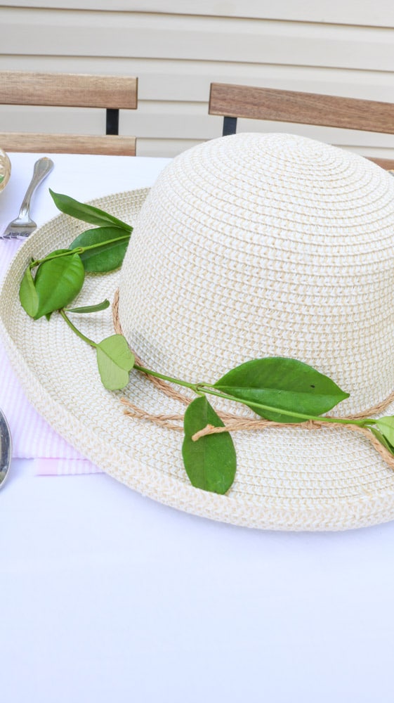 Garden party decoration ideas using a straw hat as a centerpiece with fresh green vine around the brim of the hat.