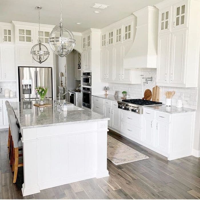 Farmhouse Kitchen by BMA 21 with a white kitchen with gray marble countertops, an oversized kitchen island and white subway tile backsplash
