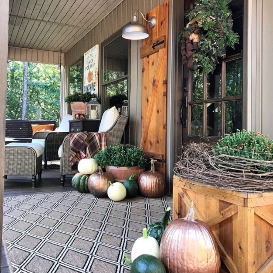 A rustic vintage fall front door and porch with a few planters of mums and metallic painted pumpkins.